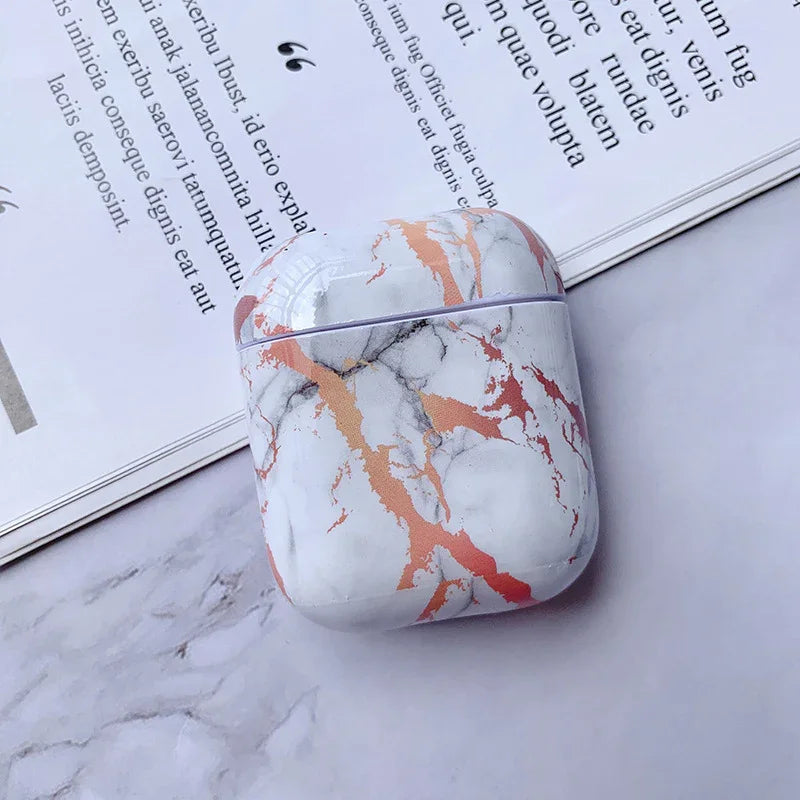 Marble pattern AirPods case with gold and pink veins on a marble surface near an open book