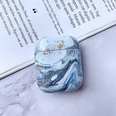 Blue marble AirPods case with gold accents on light marble background next to open book