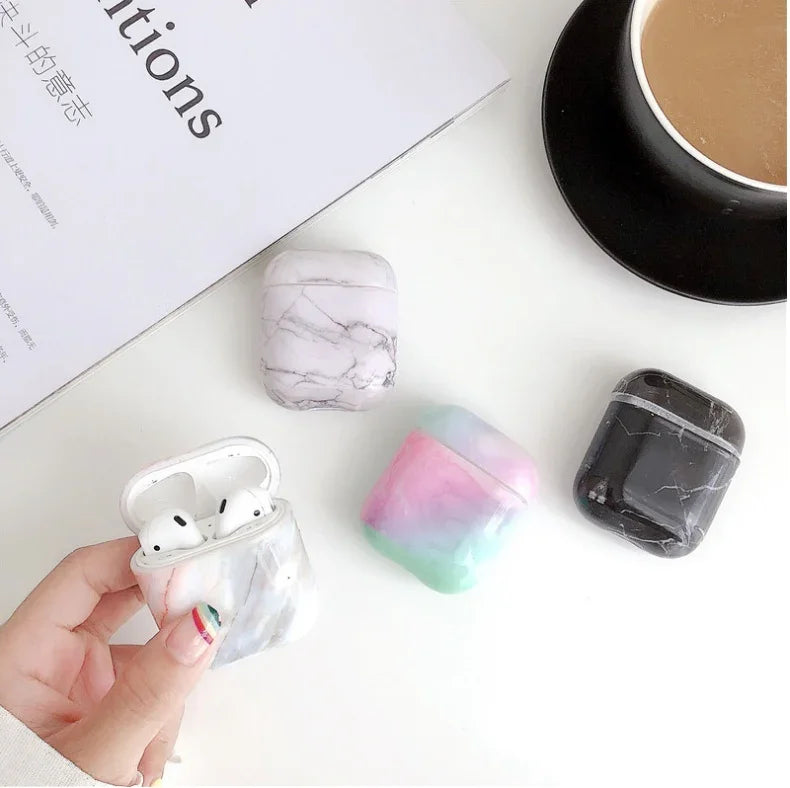 Marble and pastel AirPods cases displayed on a white desk with coffee and a magazine.