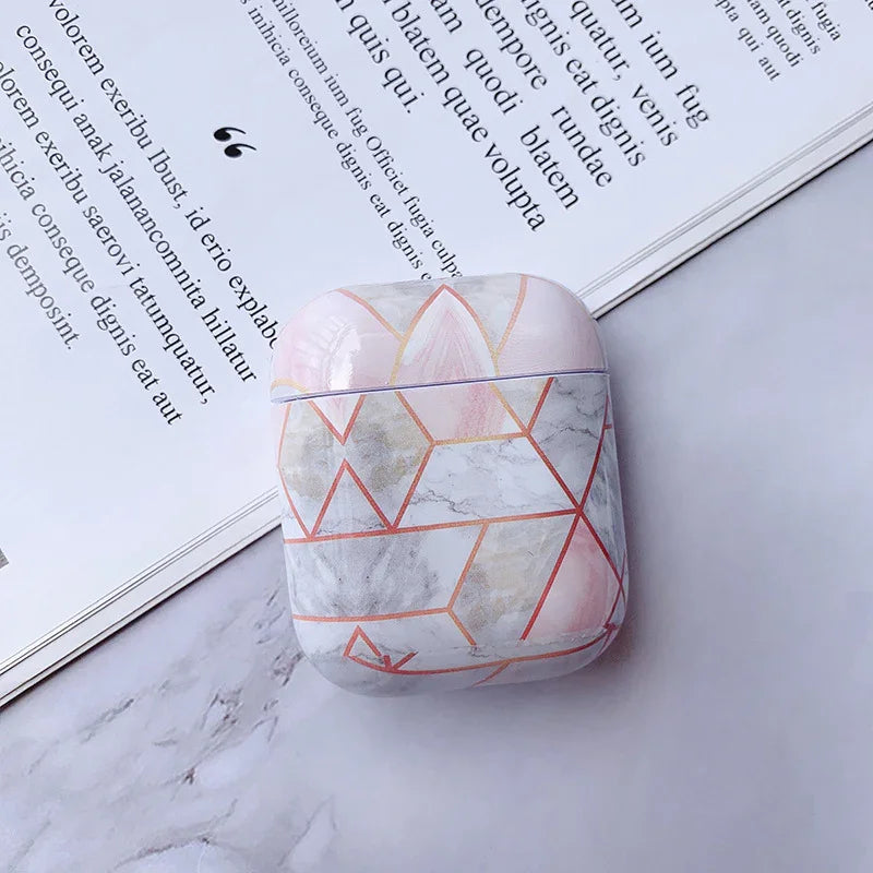 Geometric marble AirPods case with pink and gold accents on a marble surface by an open book