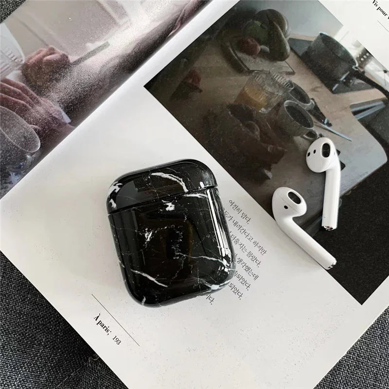 Black marble AirPods case with wireless earbuds on an open magazine page