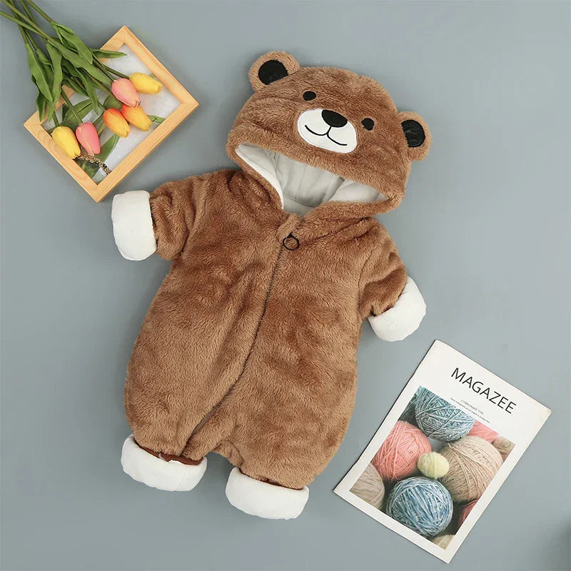 Plush brown baby bear onesie with hood, surrounded by tulips and a magazine on grey background
