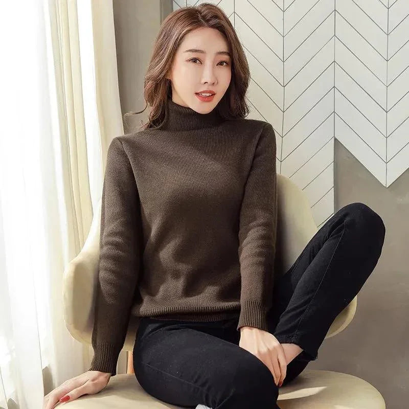 Woman wearing a brown turtleneck sweater and black pants sits on a chair indoors