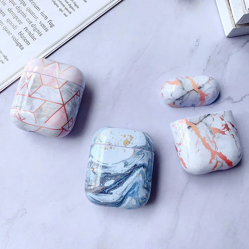 Marble pattern wireless earbud cases in pastel blue, pink, and gold on a light surface.