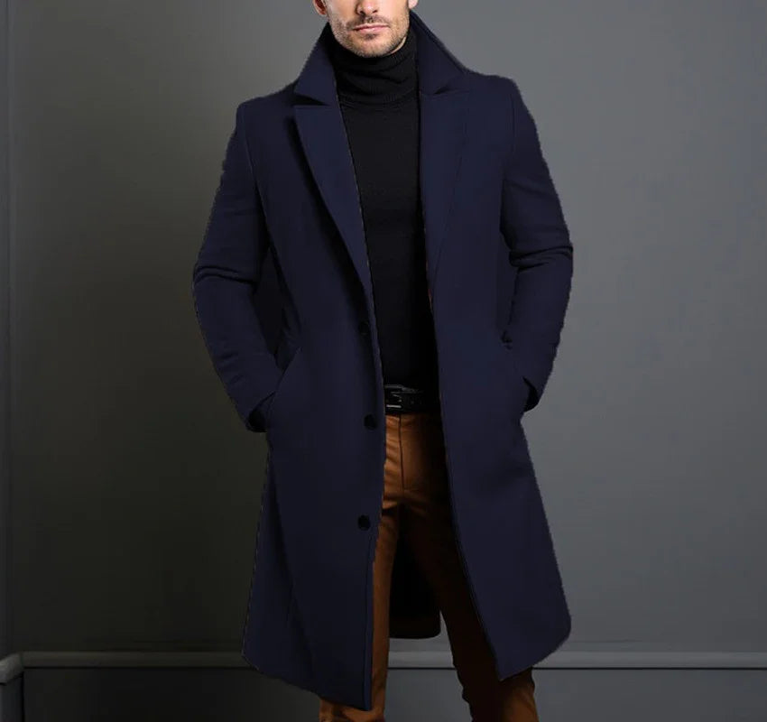 Man wearing navy overcoat, black turtleneck, and brown pants in modern setting