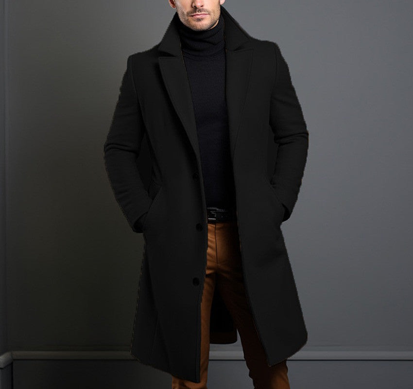 Man wearing black wool overcoat, black turtleneck, and tan pants against grey wall